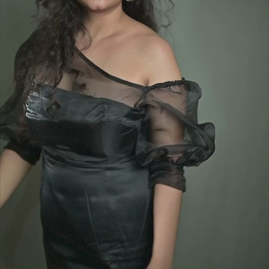 A woman wearing the Mystic Moonlit Dress with sheer organza sleeves, drop shoulders, and a sleek satin bodice, posing elegantly in a dimly lit setting.